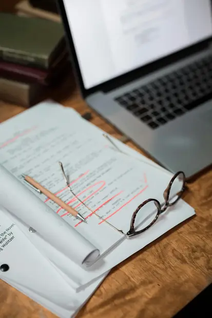 Reviewed academic paper with notes, glasses and laptop on a desk